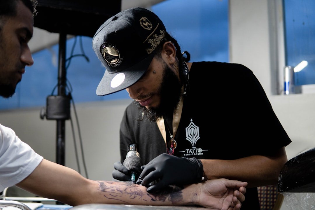 Professional tattoo artist working on a fine line design with single needle setup in a clean studio environment